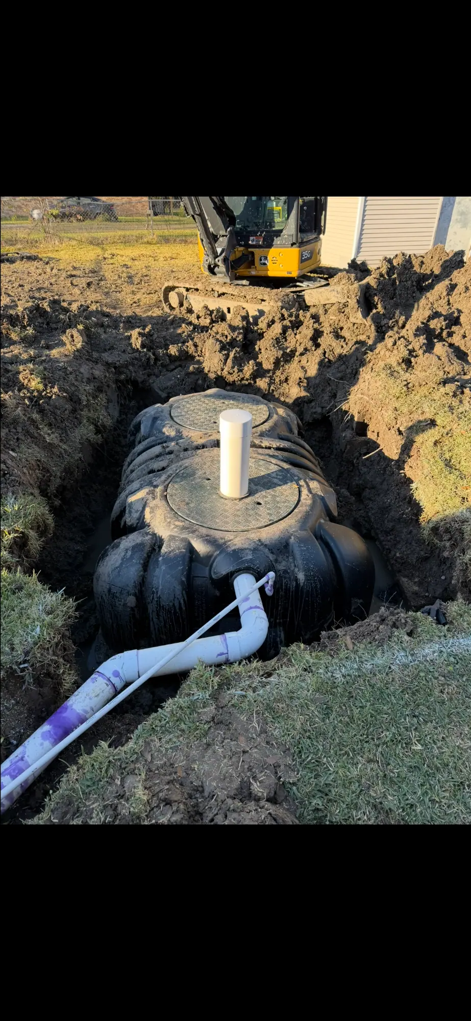 Black tank in an excavated pit with white pipe