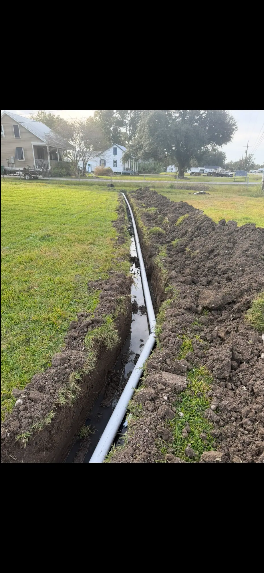 Long trench with white pipe across a lawn