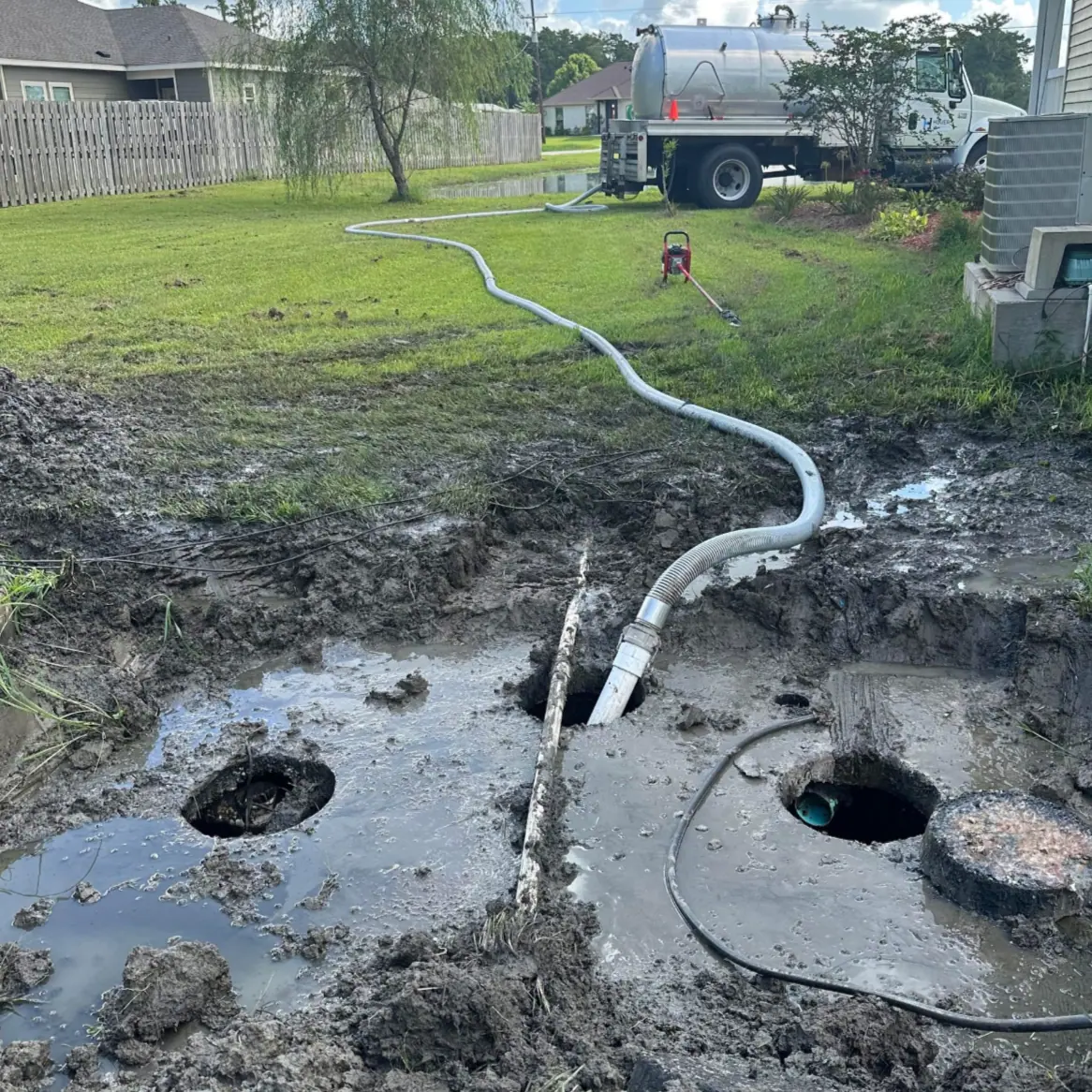 Vacuum truck and hose at open tank holes in a muddy yard